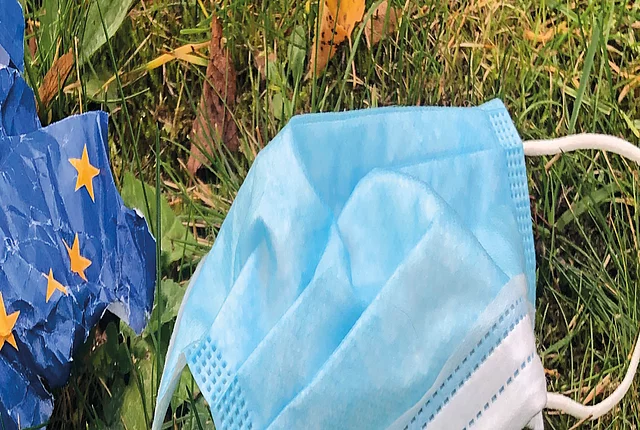 Picture of a surgical mask and a crumpled up paper depicting the European flag lying on grass