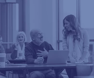 A sitting older man and a standing younger woman laugh at each other in an adult education class. 